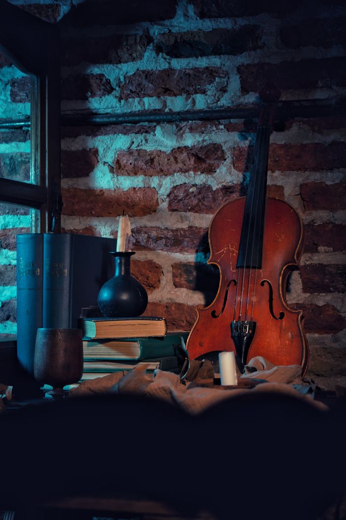 Violin with books and candle against brick wall with moody lighting. Perfect for rustic and artistic themes.