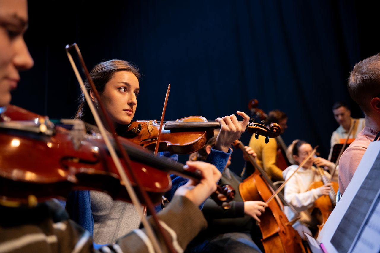 A group of musicians perform in an orchestra, featuring a violinist in focus.