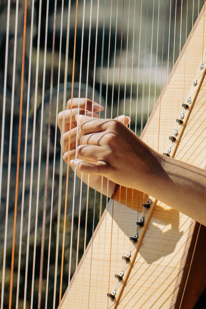 A detailed shot of hands elegantly playing a harp, emphasizing musical artistry outdoors.