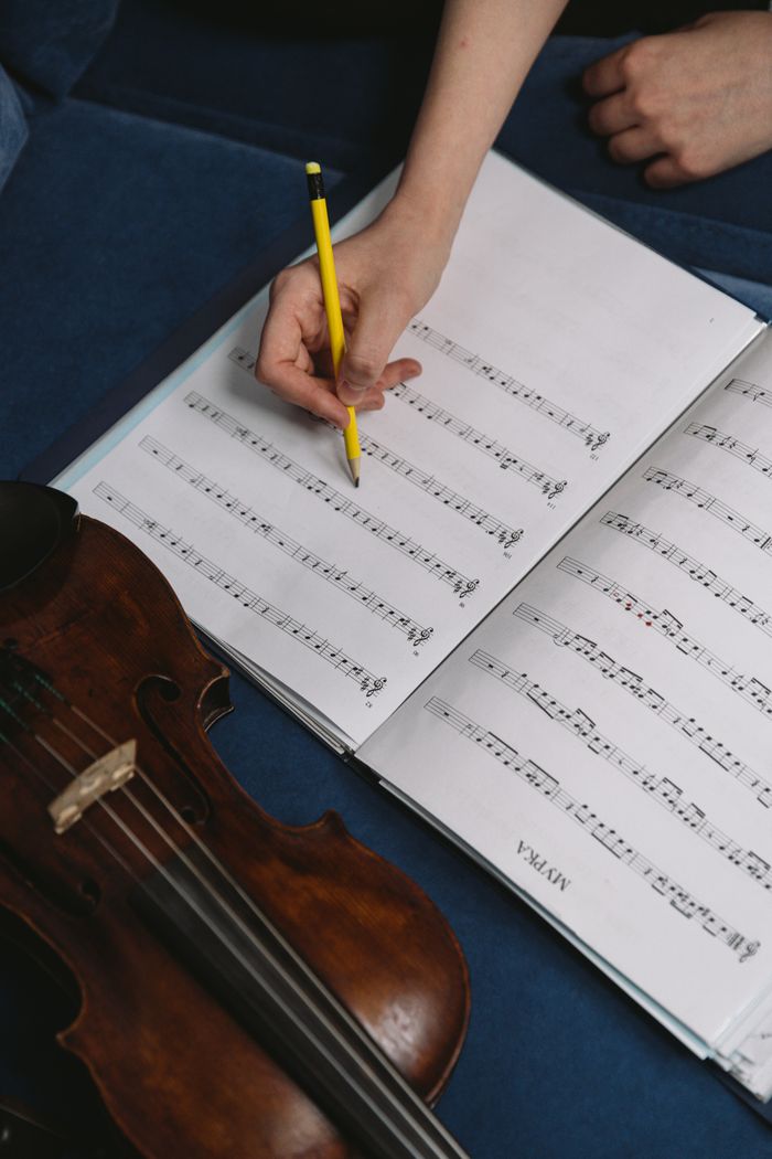 Close-up of a hand writing musical notes on sheet music with a violin beside it.